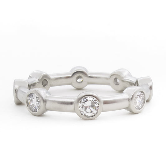 Platinum eternity band with flush bezel-set round brilliant diamonds placed at regular intervals. The minimalist design features a smooth, polished band with circular diamond settings that extend slightly outward from the ring's surface. Photographed straight-on against a white background.