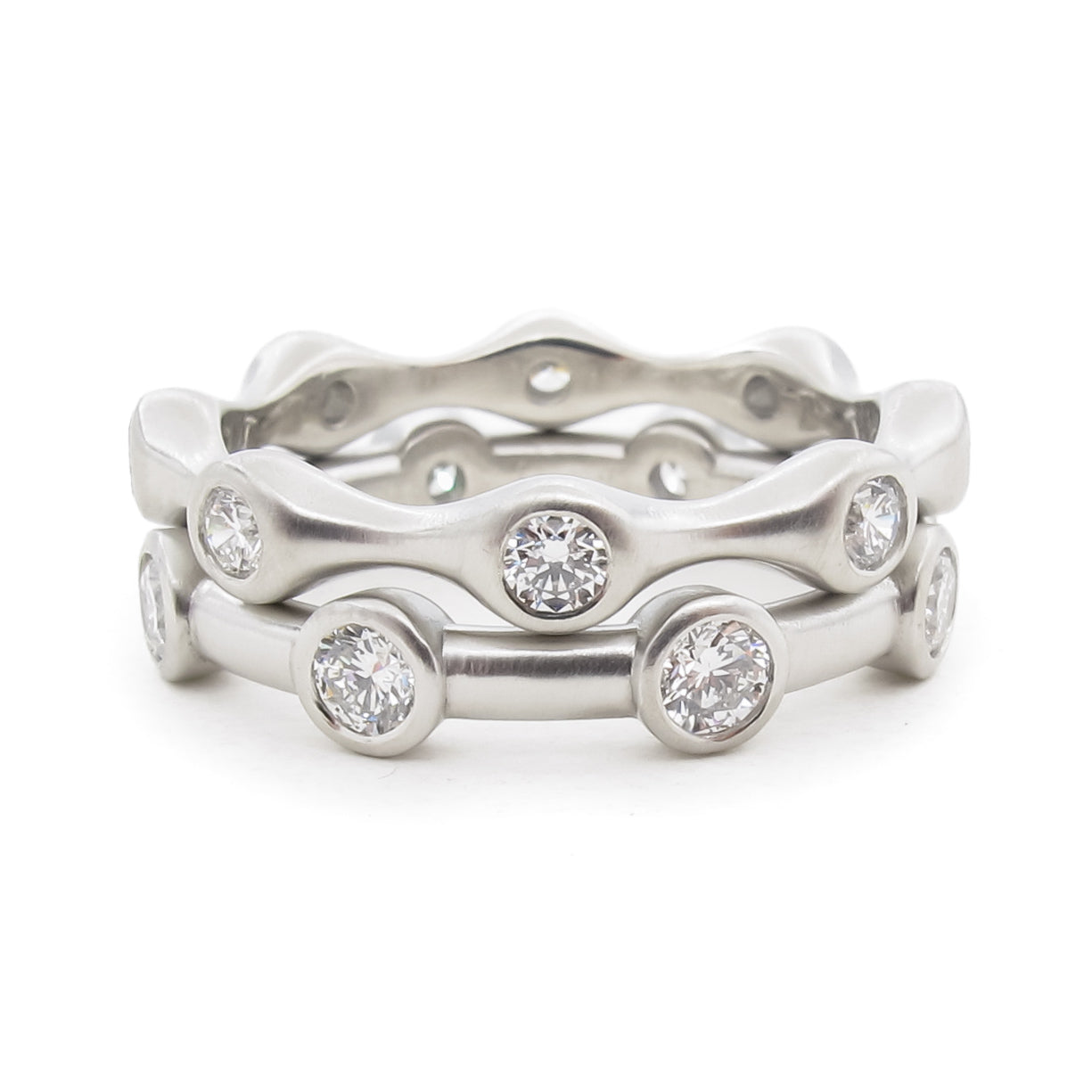 A softly curving eternity band with eight diamonds. Pure white platinum diamond eternity ring with round diamonds and matte finish. Stacked with  second eternity ring with 8 bezel set diamonds