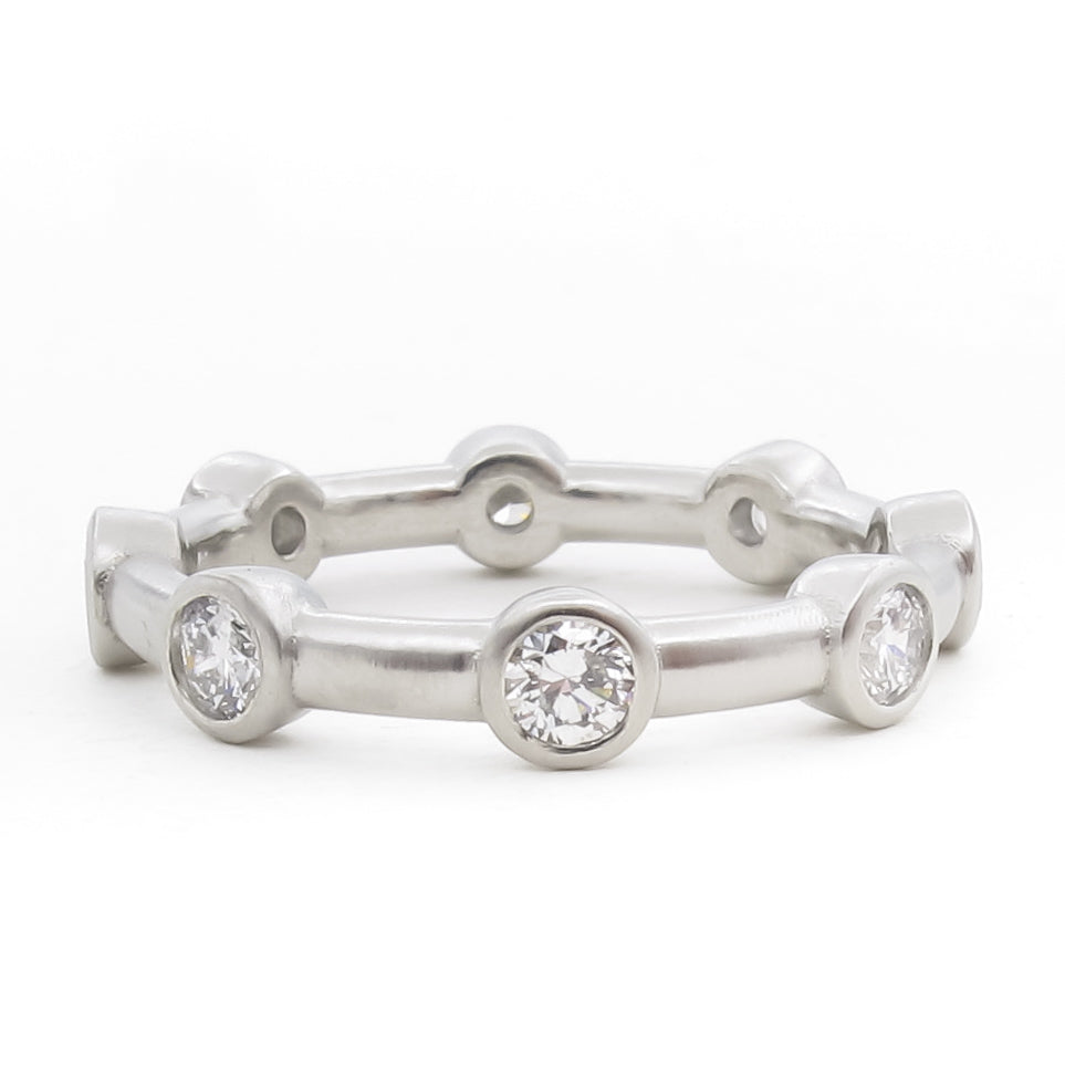 Platinum eternity band with flush bezel-set round brilliant diamonds placed at regular intervals. The minimalist design features a smooth, polished band with circular diamond settings that extend slightly outward from the ring's surface. Photographed straight-on against a white background.​​​​​​​​​​​​​​​​