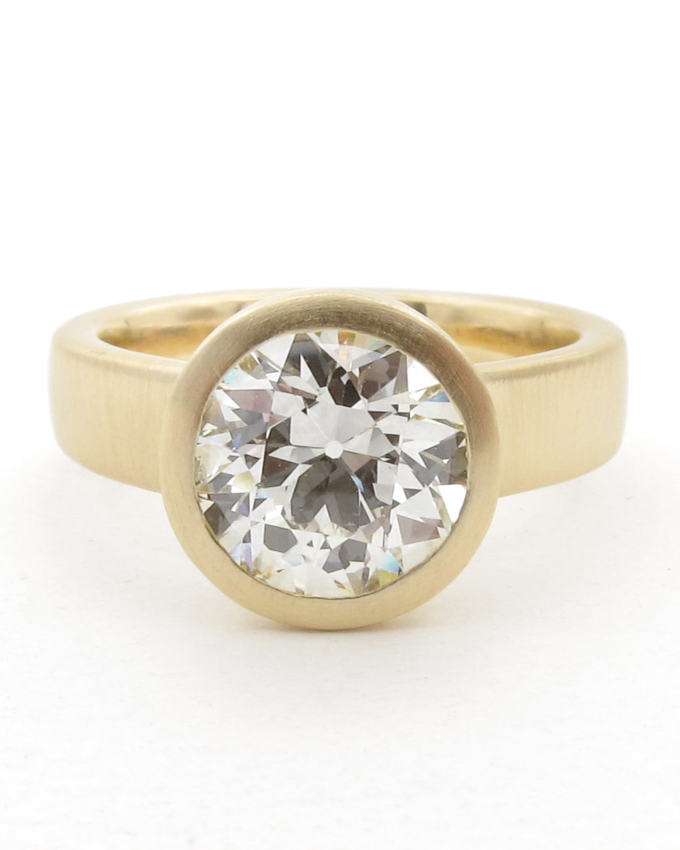 A yellow gold ring featuring a large, OEC diamond in a bezel setting, photographed against a clean white background.