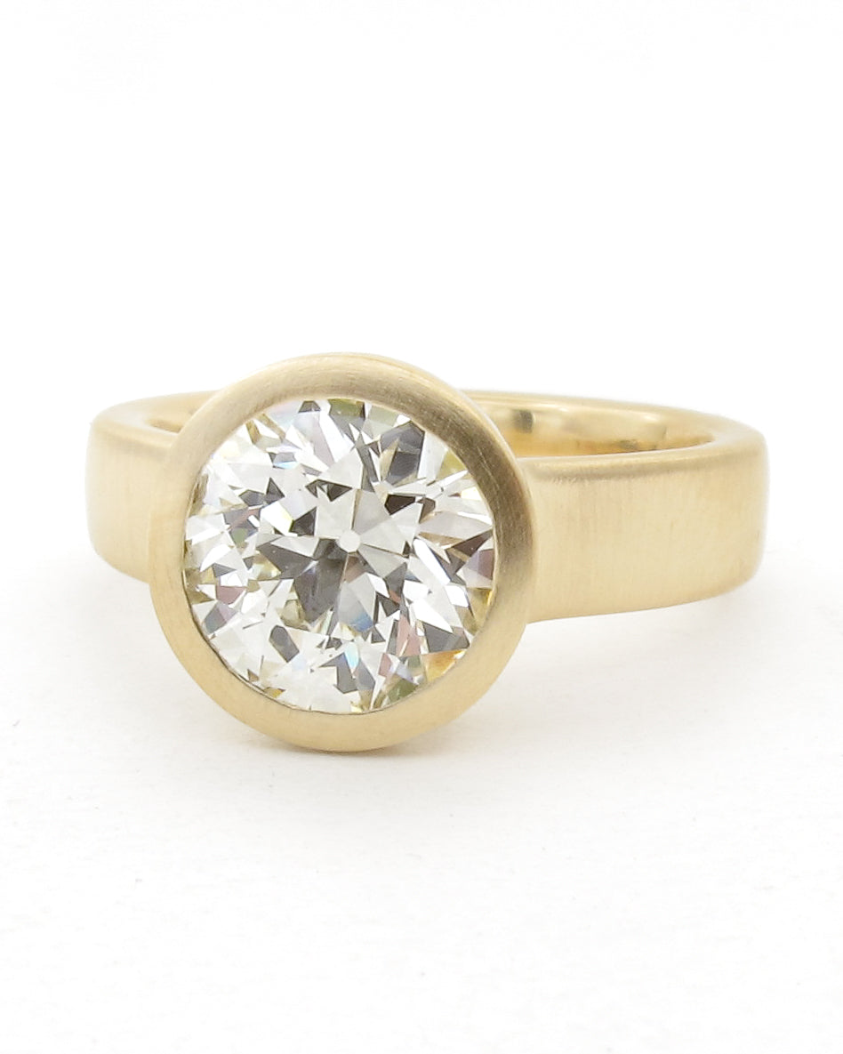 A yellow gold ring featuring a large, round OEC diamond set in a bezel setting, photographed on a clean white background.