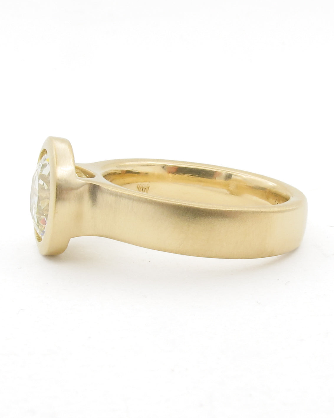 A yellow gold ring with a bezel-set clear gemstone, shown in a side profile view against a plain white background.