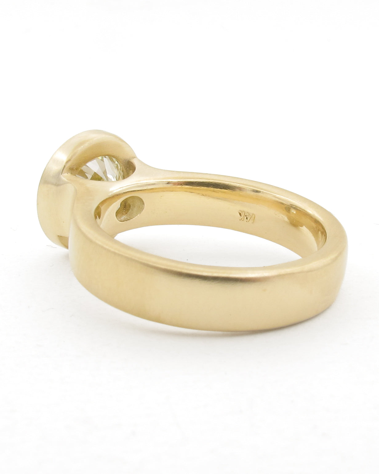 A yellow gold ring with a bezel-set diamond, shown from a side angle on a white background.