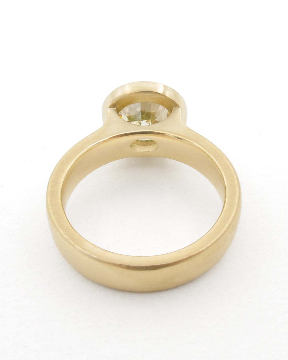 A yellow gold ring with a bezel-set round gemstone, shown from a top-down perspective on a white background.