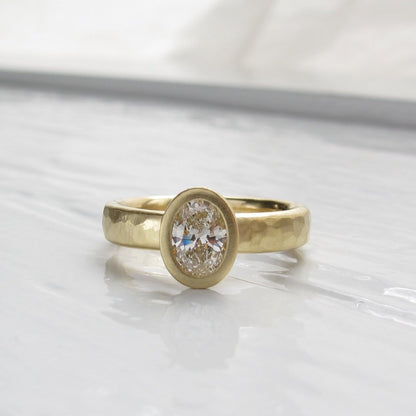 Oval diamond bezel set engagement ring with rustic hammered texture